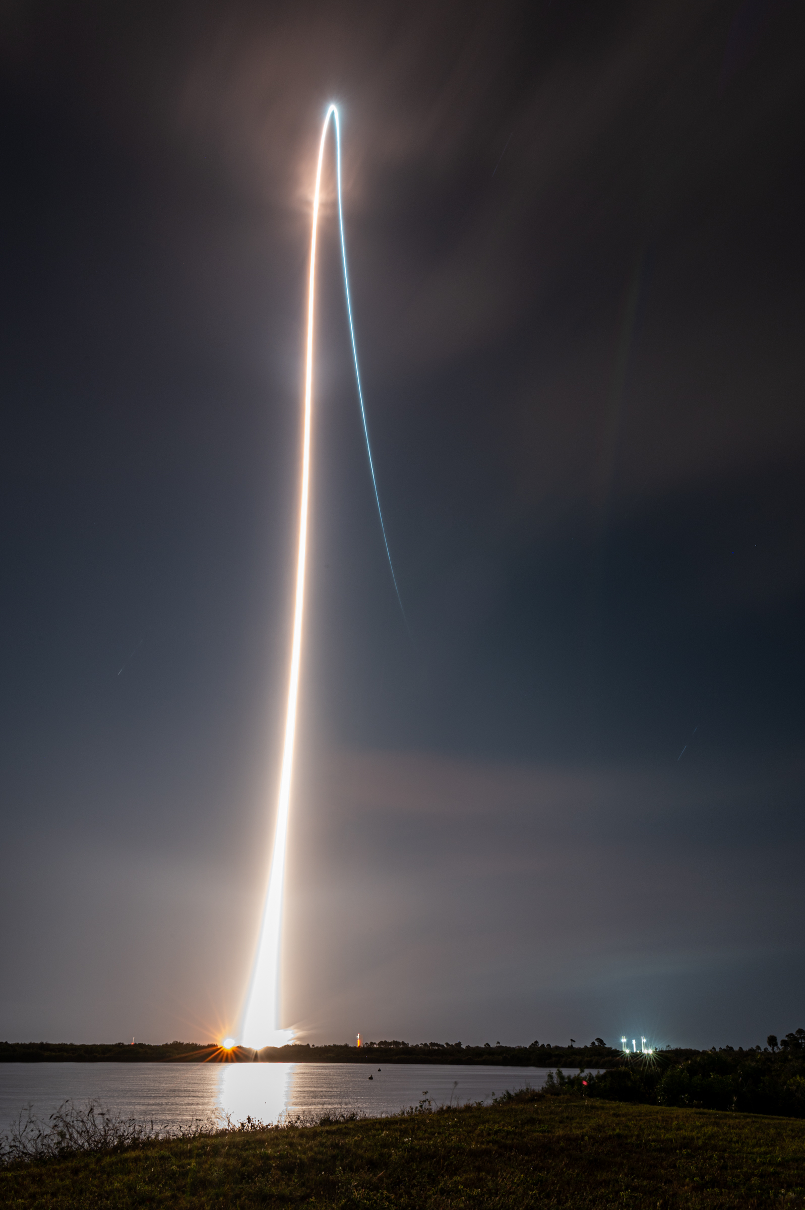 A long exposure image of Vulcan launching into a starry sky over Kennedy Space Center. The streak goes from a bright white to a blue as the SRB's burn out the boost-phase of flight continues on.