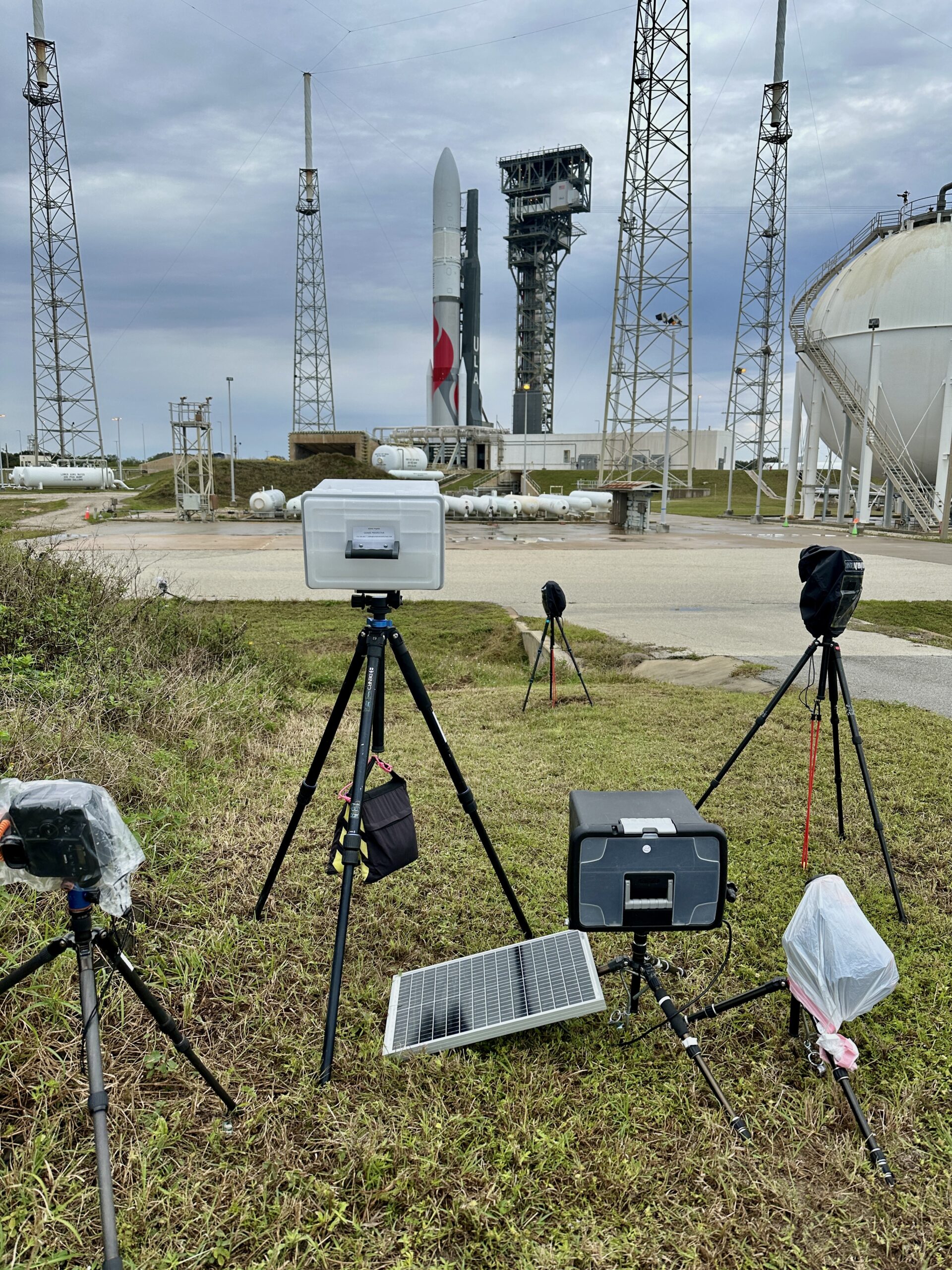 A white box on a tripod containing a Nikon DSLR is setup pointed towards the rocket at SLC-41.
